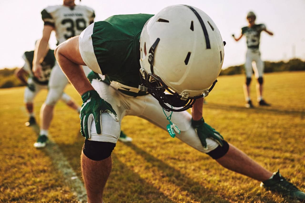 Youth football athletes running a coached agility drill on turf